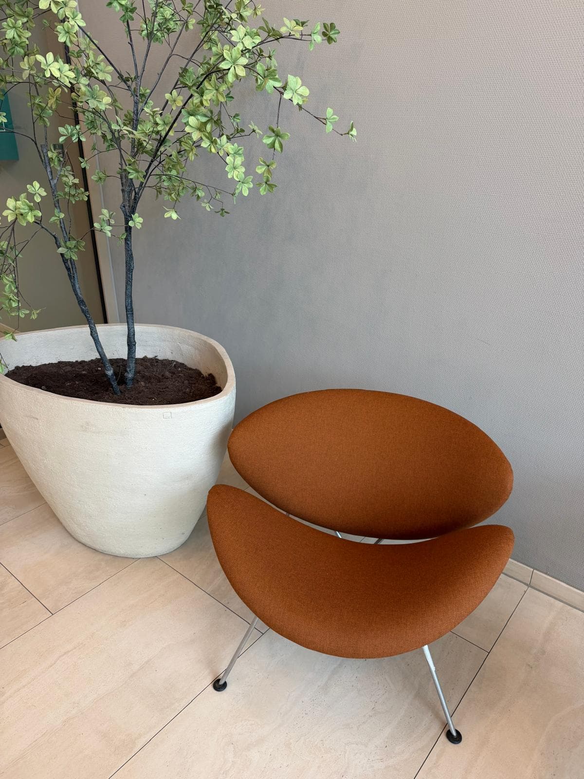 Gestoffeerde oranje designfauteuil naast een grote kamerplant