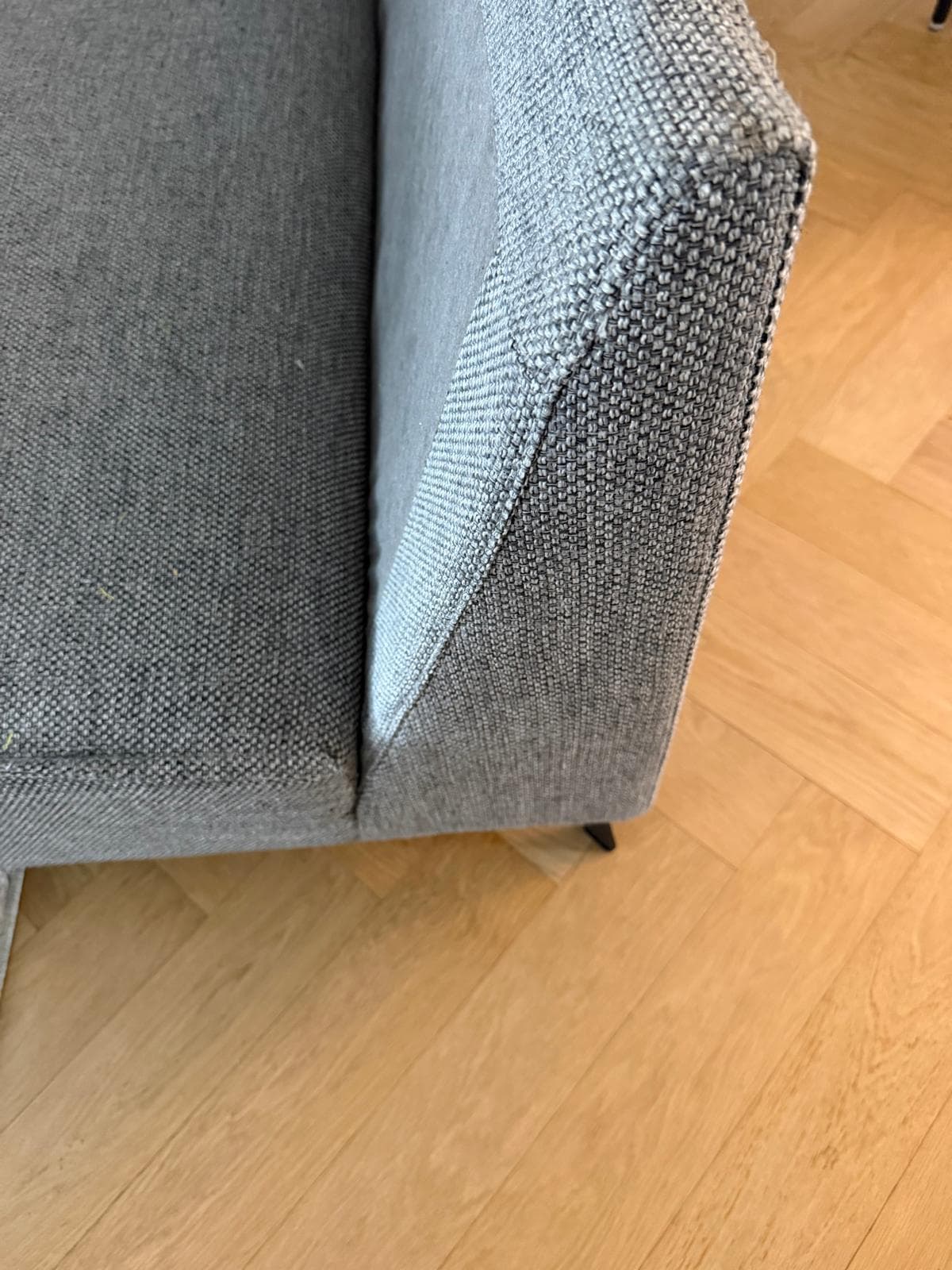 Hoek van een bank na herstel — strak opnieuw bekleed in grijze stof